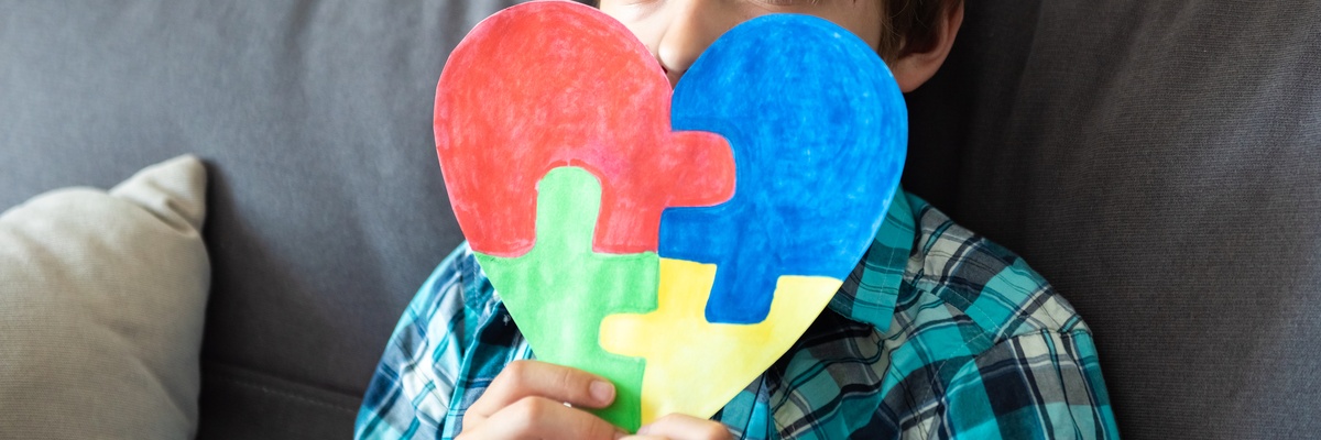 A child holding up a colourful jigsaw in a heart shape.
