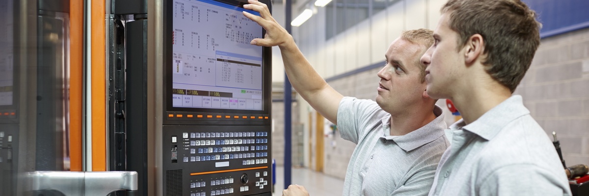An engineering technician teaches an apprentice how to use a computer system.