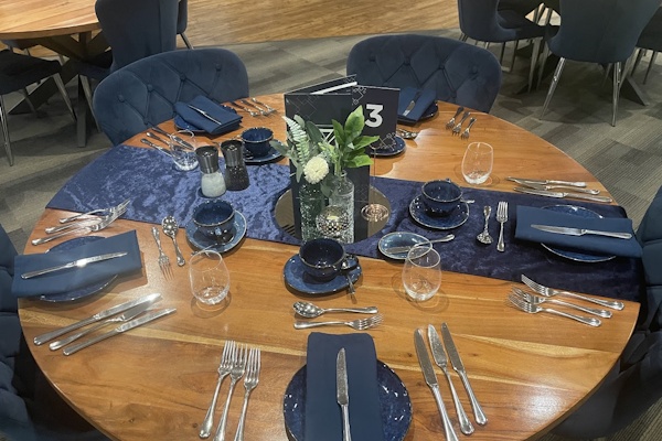 Formal event table setting with blue tableware, polished cutlery and floral centrepiece.